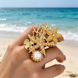 Primo piano dell'anello statement dorato con stella marina, corallo e perle eleganti.
