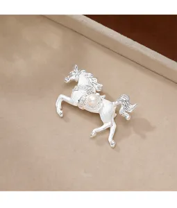 Close-up of elegant brushed silver horse brooch with a round pearl inlay on textured metal