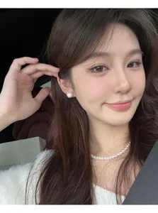 Close-up of elegant large white pearl ear clips worn by a model in a car setting.