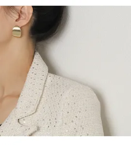 Gros plan de boucles d'oreilles géométriques minimalistes en métal doré portées par un modèle.