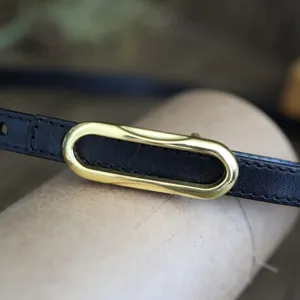 Close-up detail view of women's black leather belt with elegant gold-tone oval buckle.