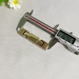 Detailed shot of gold metal belt buckle being measured with digital caliper on white fabric.