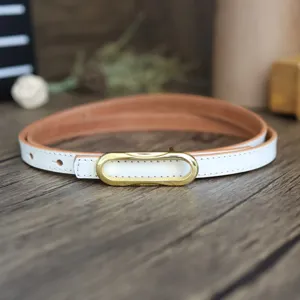 Close-up detail of a minimalist white leather belt with a sleek gold buckle on wood surface.