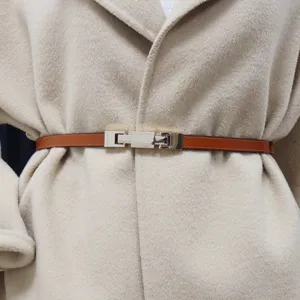 Detailed close-up shot of a slim brown leather belt with a polished metal buckle worn on a coat.