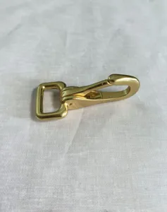 Detailopname van gouden metalen musketonhaak met vierkante basis voor tassen en sleutelhangers.