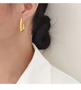 Close-up van minimalistische gouden geometrische oorringen aan het oor van een vrouw