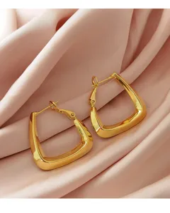 Detail van minimalistische gouden geometrische oorringen op een elegante roze zijden stof