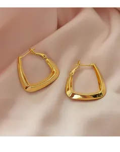 Detail van minimalistische gouden geometrische oorringen op roze satijn.