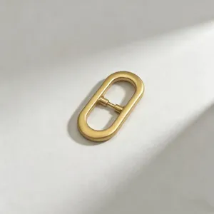 Minimalist gold oval buckle detail, elegant metallic finish for bag and belt accessories.