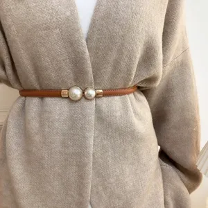Detailopname van een minimalistische dunne bruine lederen riem met elegante dubbele parel.