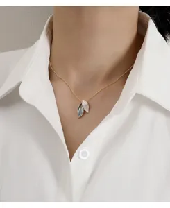 Close-up of golden leaf pendant necklace with white and grey enamel detail