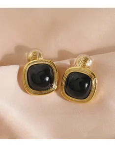 Detailansicht von Vintage-Clip-Ohrringen in Gold mit schwarzem Stein auf Seidenstoff.