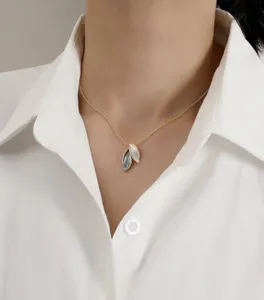 Elegant gold leaf pendant necklace with contrast colors worn by a model in white.