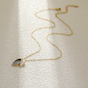 Gold leaf pendant necklace with contrasting enamel leaves on a minimalist textured surface