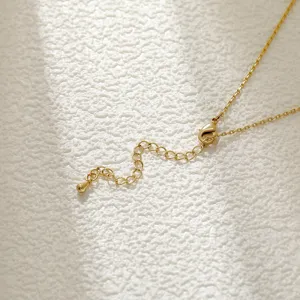 Detailed view of a golden necklace clasp and extension chain on a textured stone surface