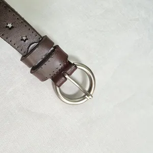 Close-up detail of women's brown leather belt featuring star cutouts and silver round buckle.