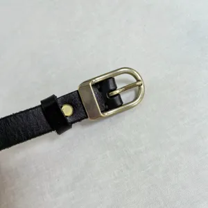 Close-up detail of a black leather strap with a metallic pin buckle and metal rivet fastener.