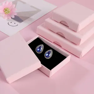 Détail de la boîte à bijoux rose avec boucles d'oreilles larmes bleues sur velours noir.