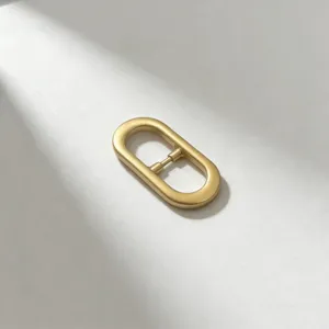 Minimalist oval metal belt buckle detail view, elegant golden matte finish for women's apparel.