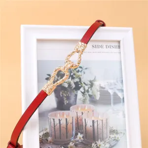 Close-up detail of red leather belt with elegant gold-tone twisted metal knot buckle accessory.
