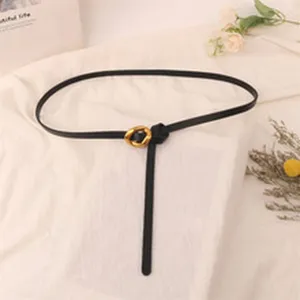 Details of stylish thin black leather belt with irregular gold metal buckle knot accessory.