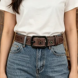 Close-up of a women's brown leather belt featuring floral cut-outs worn on blue denim jeans