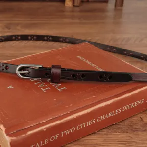 Detail view of a genuine leather thin belt with cutout design and silver buckle, retro style.