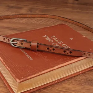 Close up of genuine leather thin waist belt featuring delicate cutouts on vintage book.