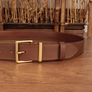 Close-up of a classic brass square buckle on a high-quality brown leather belt.