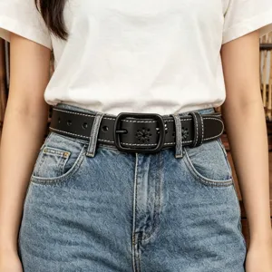 Close-up shot of a stylish black leather belt with floral cutouts worn with blue denim jeans