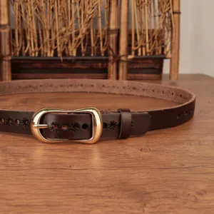 Dettaglio di cintura in pelle marrone, intaglio floreale con fibbia dorata su legno.