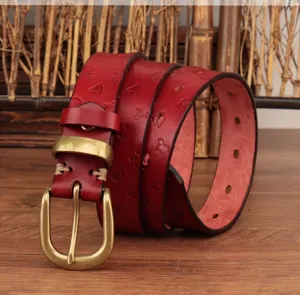 Detalle de cinturón de cuero rojo con hebilla de latón vintage y motivos náuticos grabados.