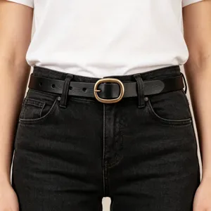 Detail view of minimalist black leather belt with vintage brass oval buckle on denim.