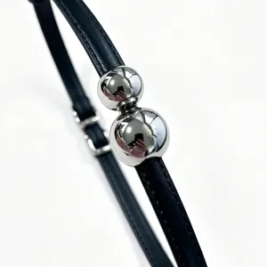 Close-up detail of silver spherical beads on a slim black leather belt with fine stitching.