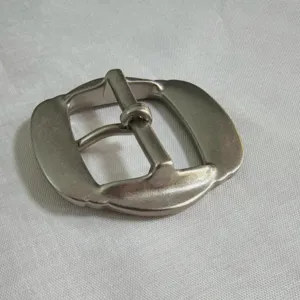 Close-up detail shot of a vintage silver zinc alloy belt pin buckle, showing fine texture.