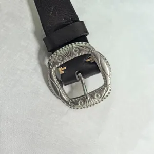 Leather belt detail showing vintage silver metal buckle with intricate floral engraving.