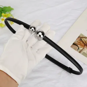 Detail view of black skinny belt with asymmetrical silver ball buckle on white glove.
