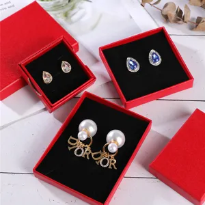Détail de boîtes à bijoux rouges avec intérieur en velours noir et boucles d'oreilles variées.