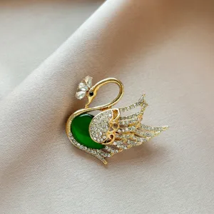 Elegant swan brooch for women featuring sparkling crystals and a green stone. Perfect chic accessory.