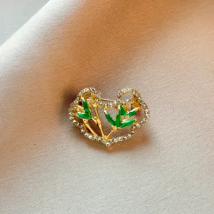 Detailed close-up of a golden heart brooch adorned with green enamel and clear rhinestones.