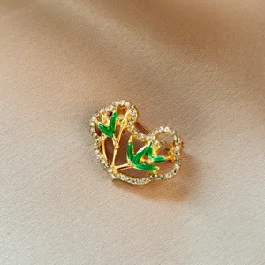 Close-up detail of vintage gold ruyi lock brooch with sparkling rhinestones and green bamboo.