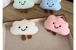 Gros plan de quatre pendentifs et broches nuages en peluche dans un plateau crème