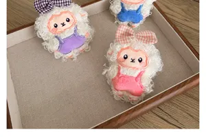 Gros plan de mignonnes broches mouton en peluche blanche avec salopettes colorées.