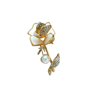 Elegant gold tone rose brooch decorated with sparkling rhinestones and a pearl pendant.