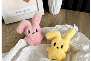 Gros plan de deux adorables lapins en peluche rose et jaune sur du papier froissé.