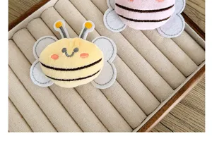 Vue détaillée de breloques abeilles en peluche sur un présentoir à bijoux en velours.