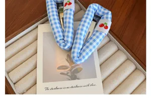 Gros plan détaillé de barrettes à carreaux bleus et blancs avec écussons cerise.