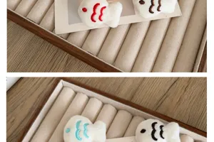 Close-up of plush fish brooches with colorful embroidery details in a jewelry display tray.
