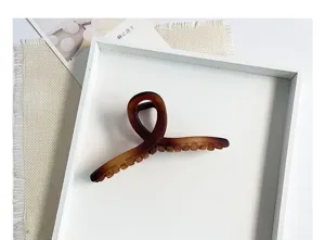 Vue détaillée d'une grande pince à cheveux mate marron dans un plateau blanc minimaliste chic.