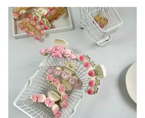 Detailansicht süßer Haarklammern mit Pfirsich-, Rosen- und Schleifendesigns in einem Minikorb